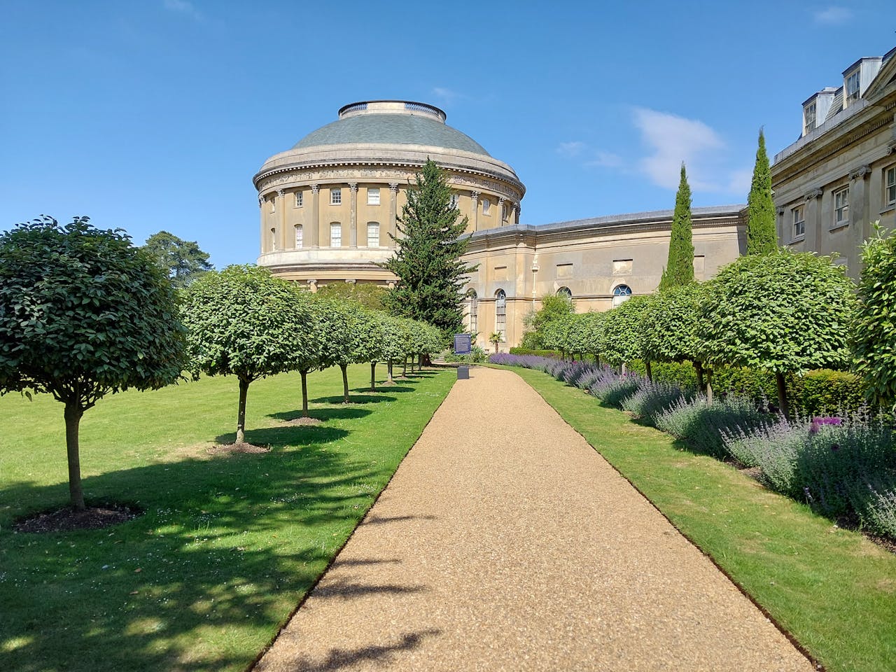 services-hero A scenic garden with manicured trees and a historic domed building under a clear blue sky.